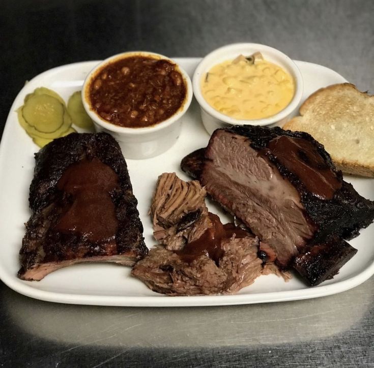 a white plate topped with ribs, beans and bread