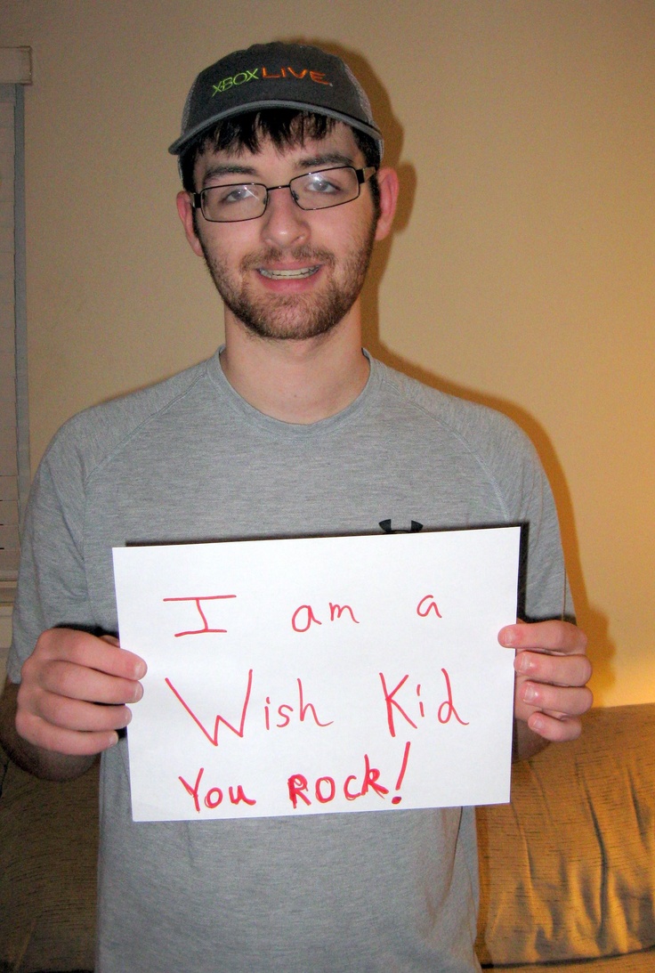 a man holding up a sign that says i am a wish kid you rock