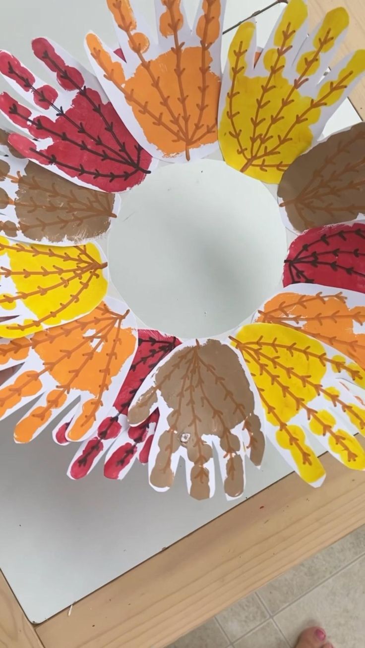 paper flowers are arranged in a circle on a table with someone's hand prints