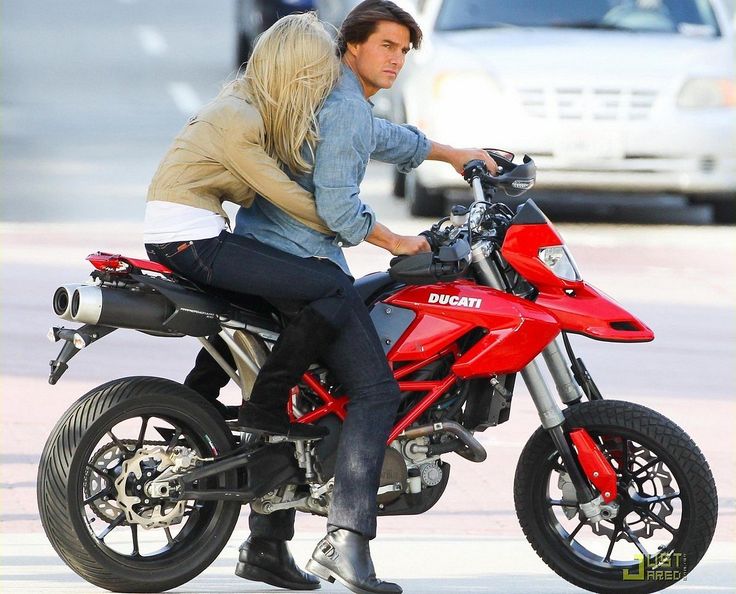 a man riding on the back of a red motorcycle next to a blonde haired woman