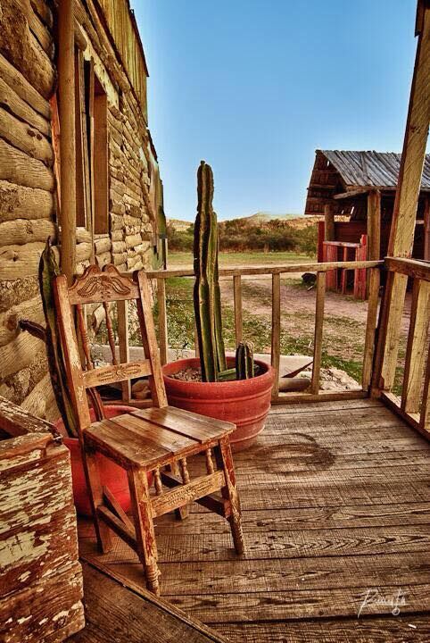 a wooden chair sitting on top of a porch next to a potted cacti