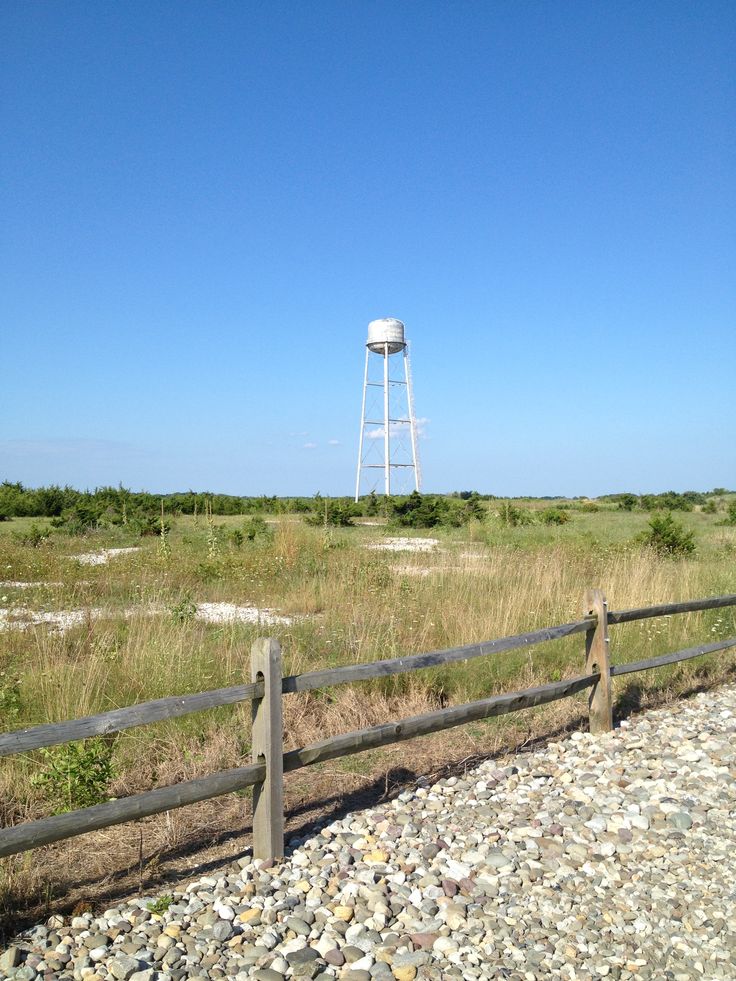 a water tower is in the distance behind a wooden fence and some rocks on the ground