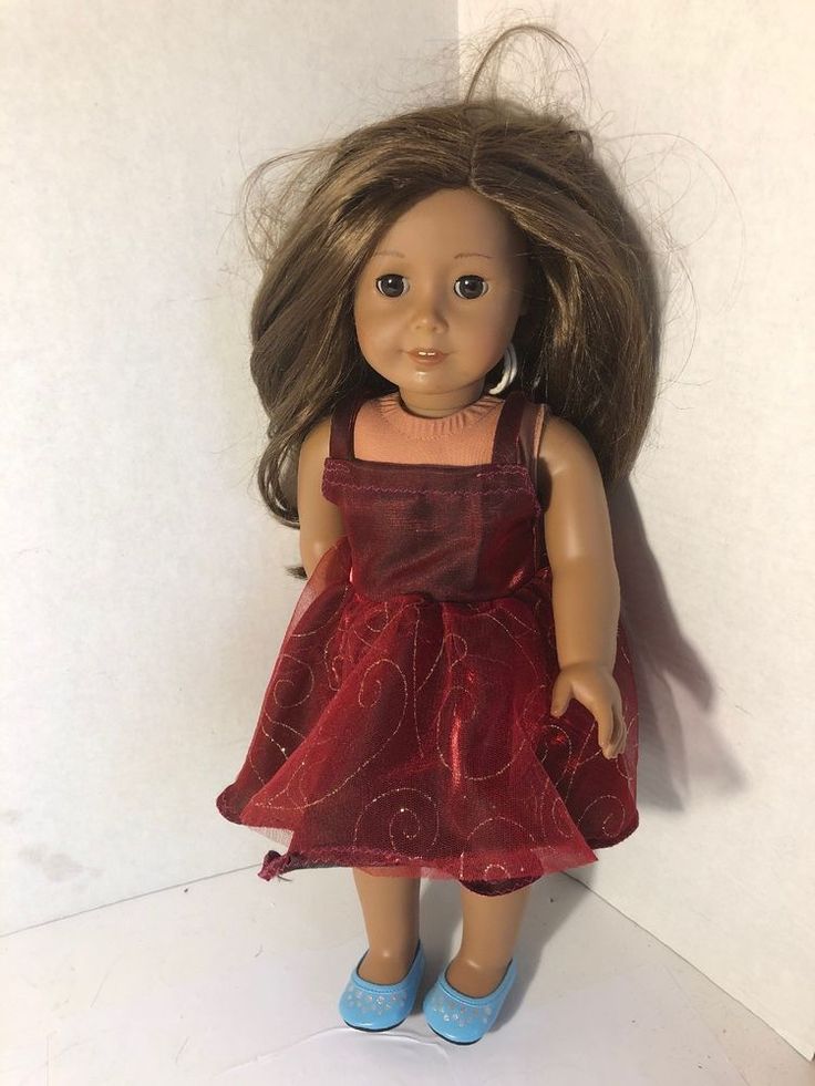 a doll with brown hair wearing a red dress and blue shoes is standing on a white surface