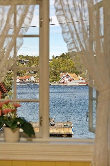 the view from an open window looking out onto a body of water with houses in the distance