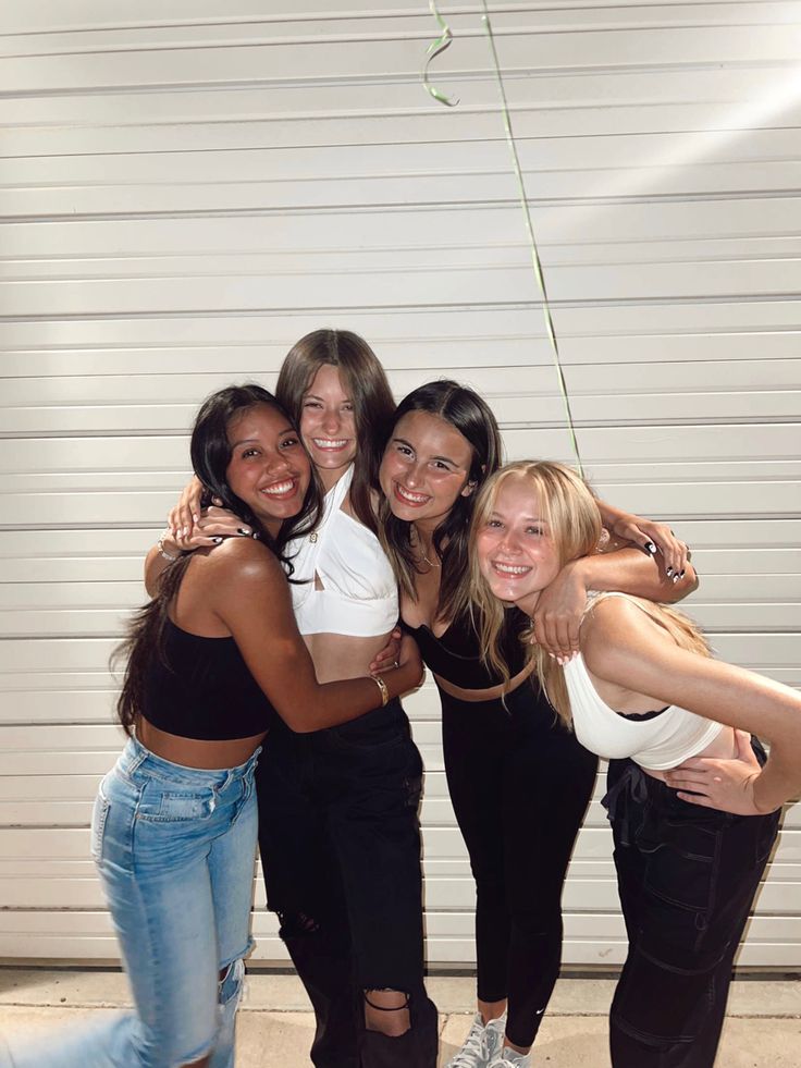 four young women are posing together for a photo in front of a white garage door