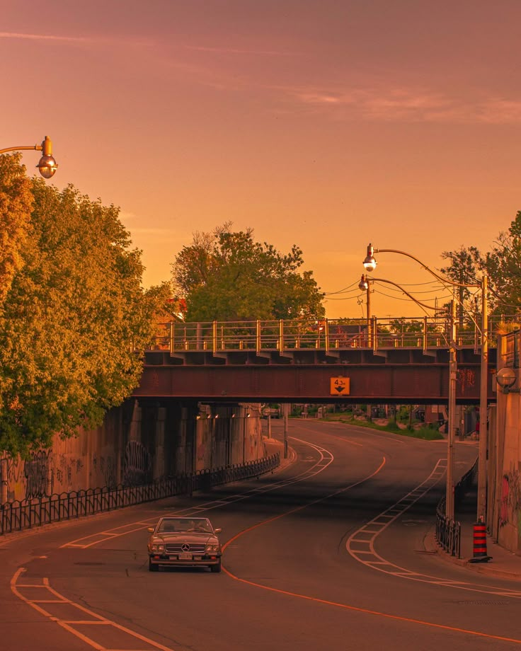 the car is driving down the road under an overpass at sunset or sunrise time