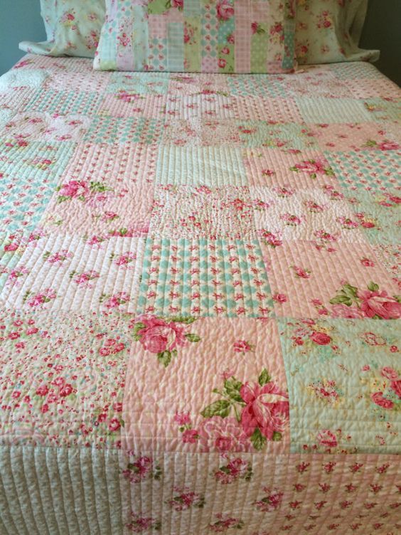 a pink and green quilted bed with flowers on it's headboard, along with two pillows