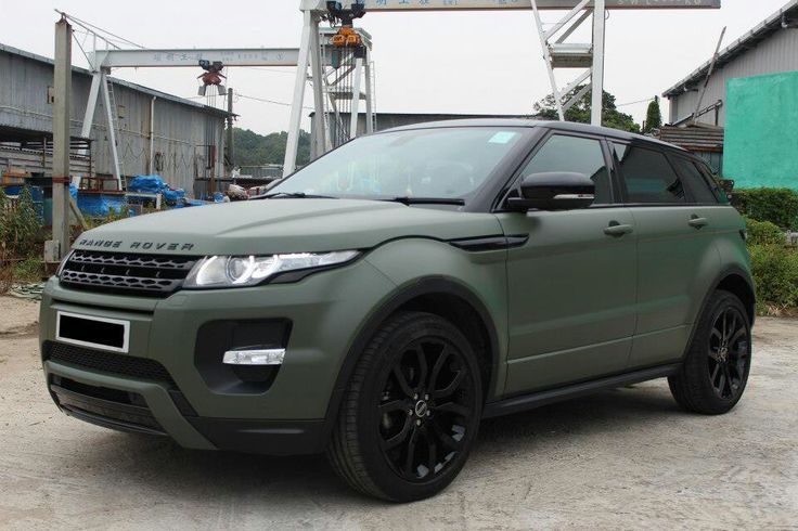 a green range rover is parked in front of some buildings and trees with an overhead crane behind it