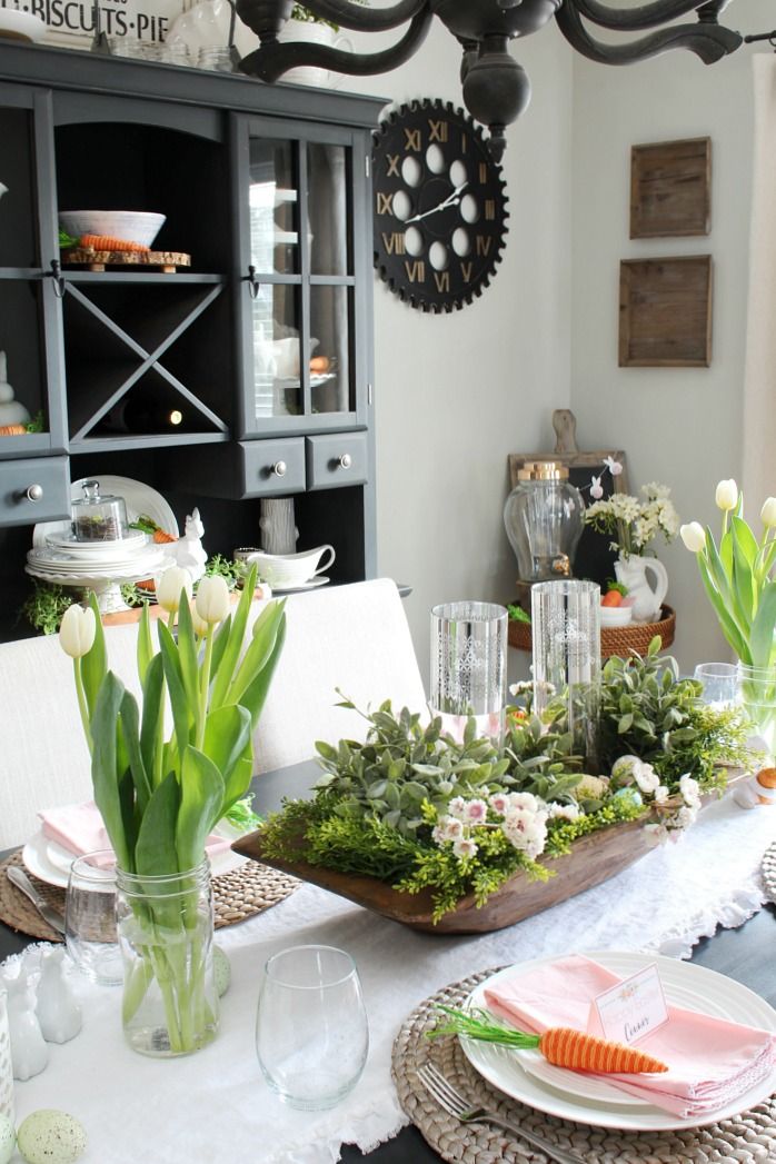 a dining room table is set with flowers and greenery for the centerpieces