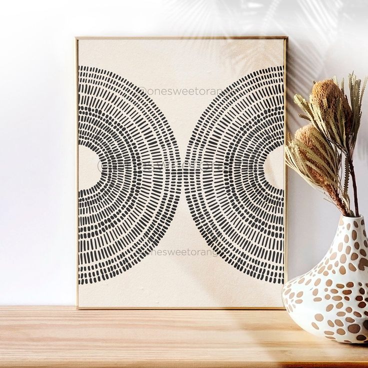 a vase with some dried flowers in it next to a wall mounted art piece on a shelf