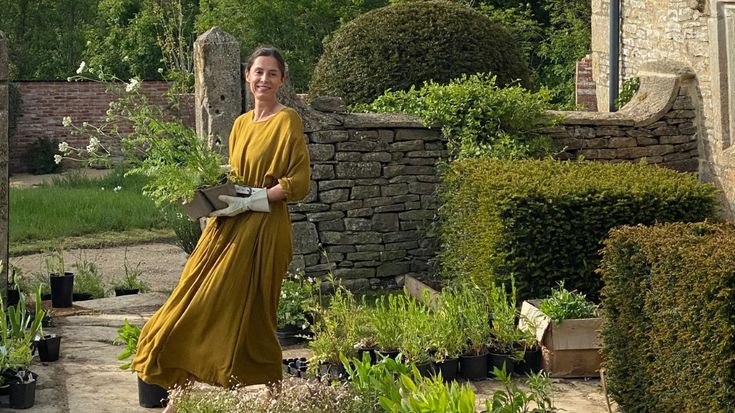 a woman in a yellow dress is walking through the garden with potted plants on either side