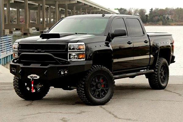 a large black truck parked next to a body of water in front of a building