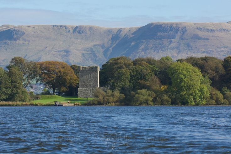 an old castle sits on the shore of a lake with mountains in the back ground