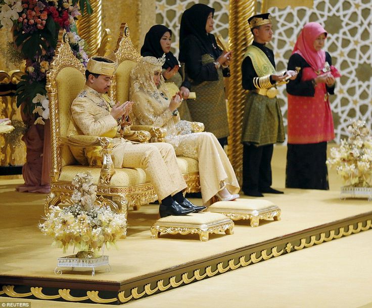 a man and woman sitting on a golden chair in front of other people wearing traditional garb