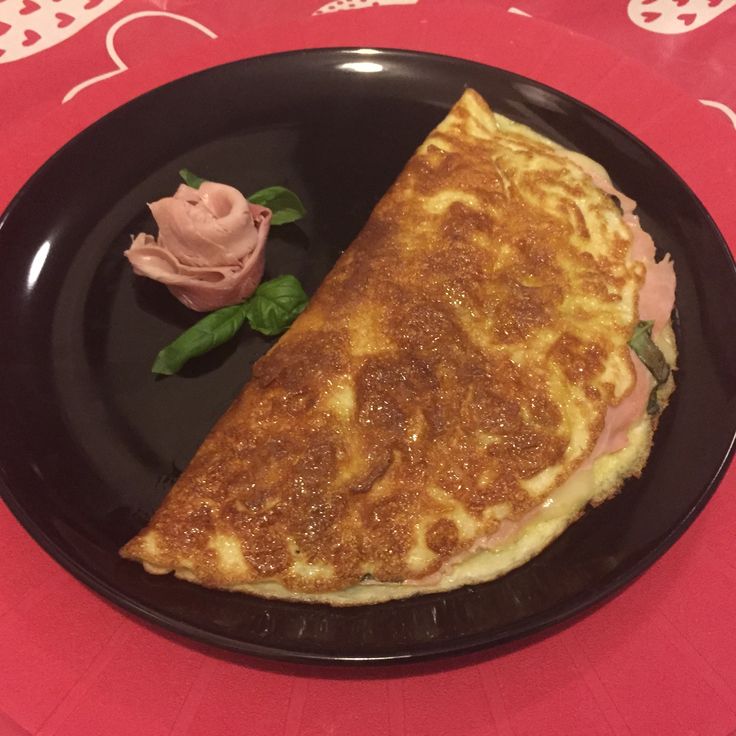 a black plate topped with an omelet next to a small flower on a red table cloth