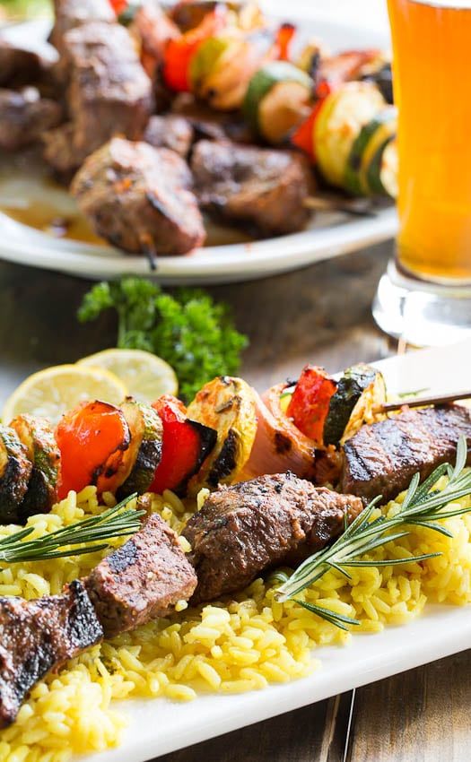 two plates with meat and veggies on them next to a glass of beer