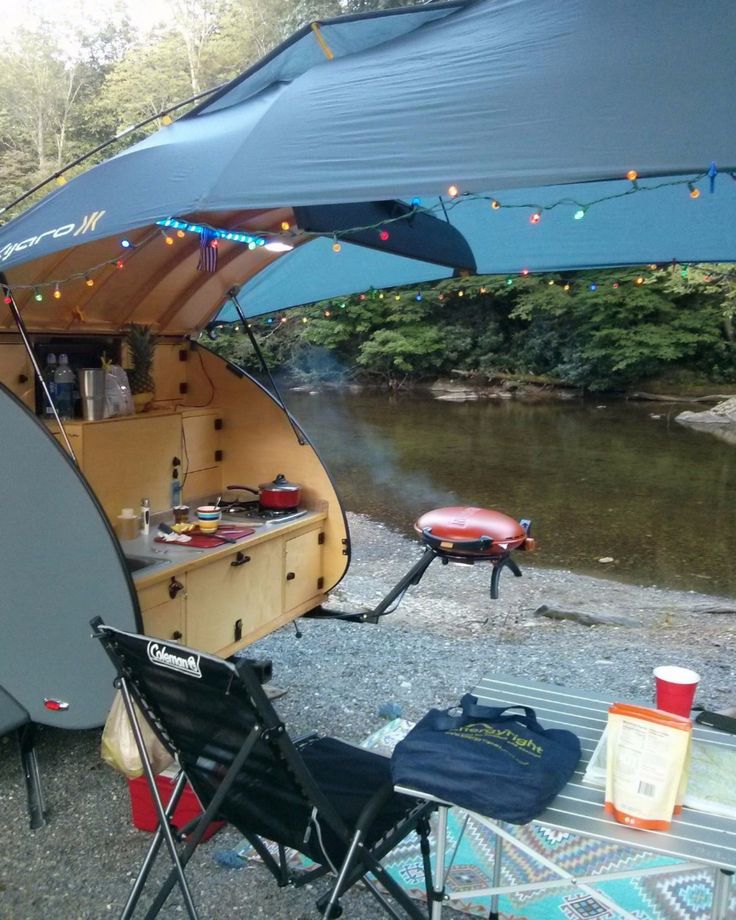 a camper trailer is set up on the shore with an awning over it