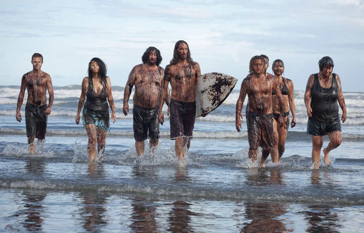 a group of men walking on top of a beach next to the ocean holding a surfboard