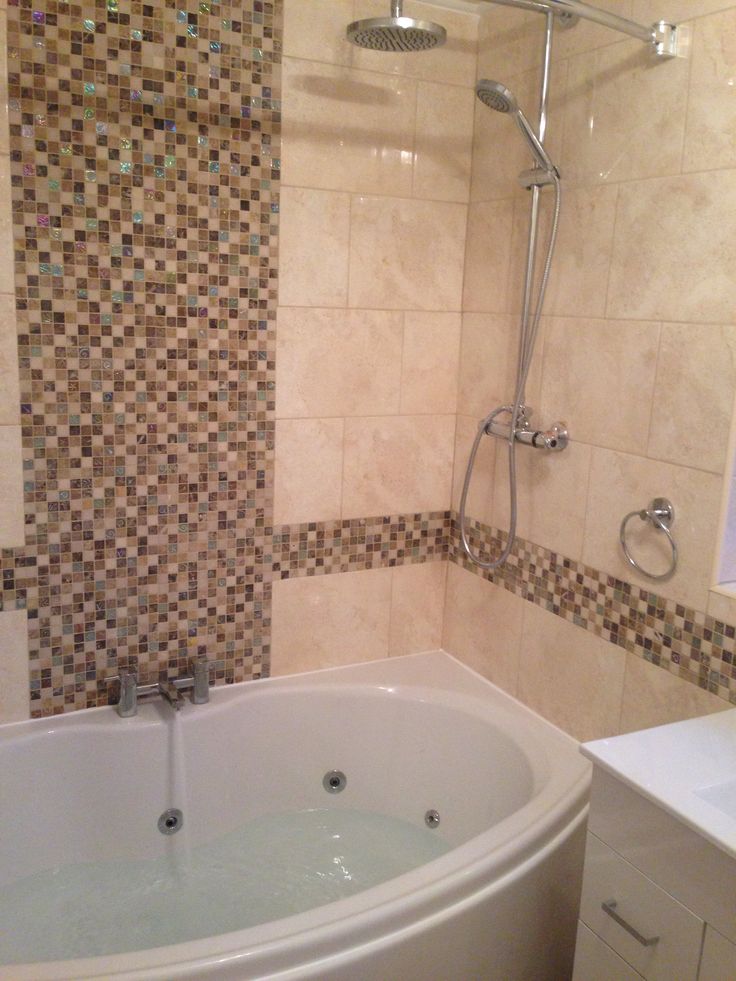 a bath tub sitting next to a shower head in a tiled bathroom with brown and white tiles on the walls