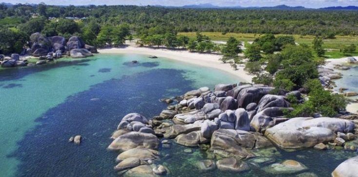 an aerial view of the beach and water near some rocks in the ocean with trees around it