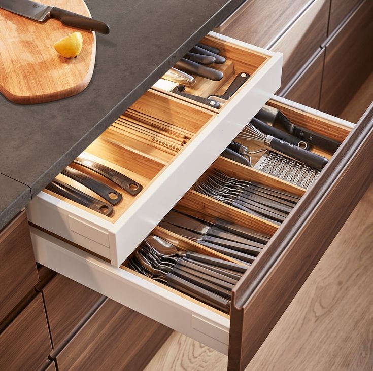 an open drawer in a kitchen filled with utensils and cutting board on top of a counter