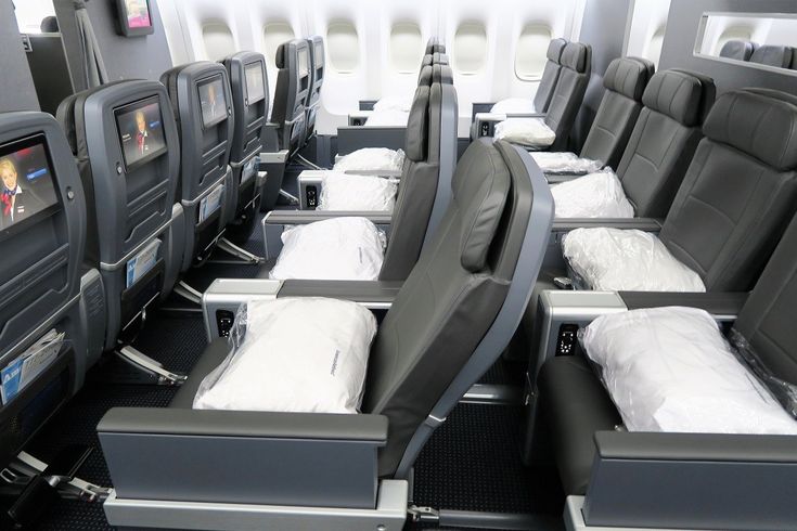 rows of empty seats in an airplane with televisions on the back wall and windows