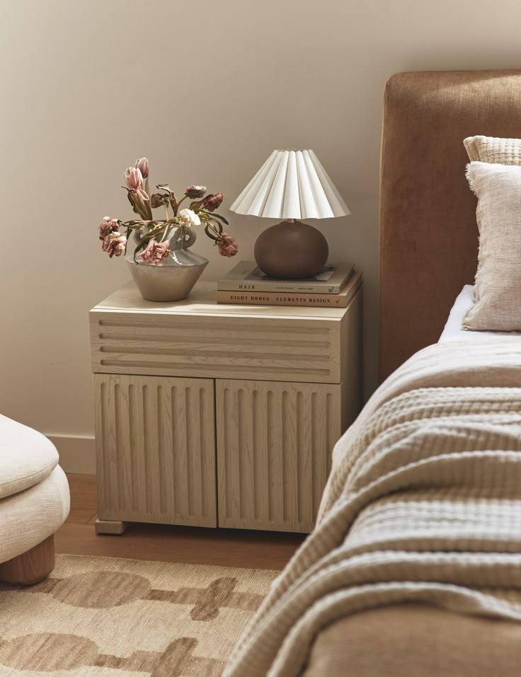 a bedroom with a bed, nightstand and lamp on it's side table in front of a white wall