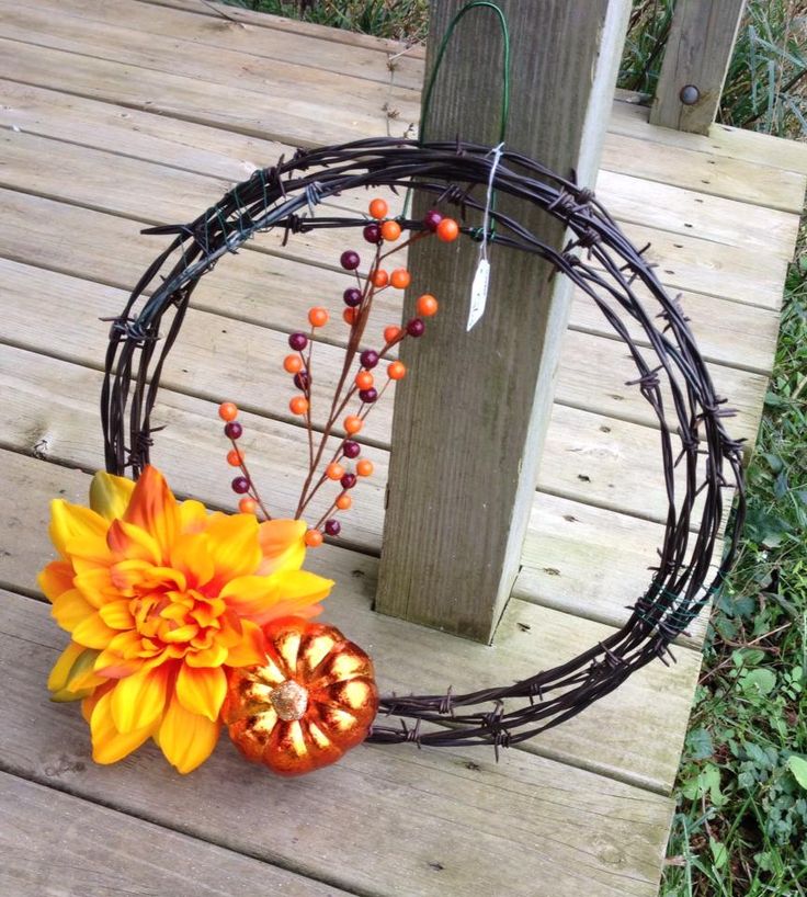 an orange and yellow flower sitting on top of a wooden floor next to a wreath