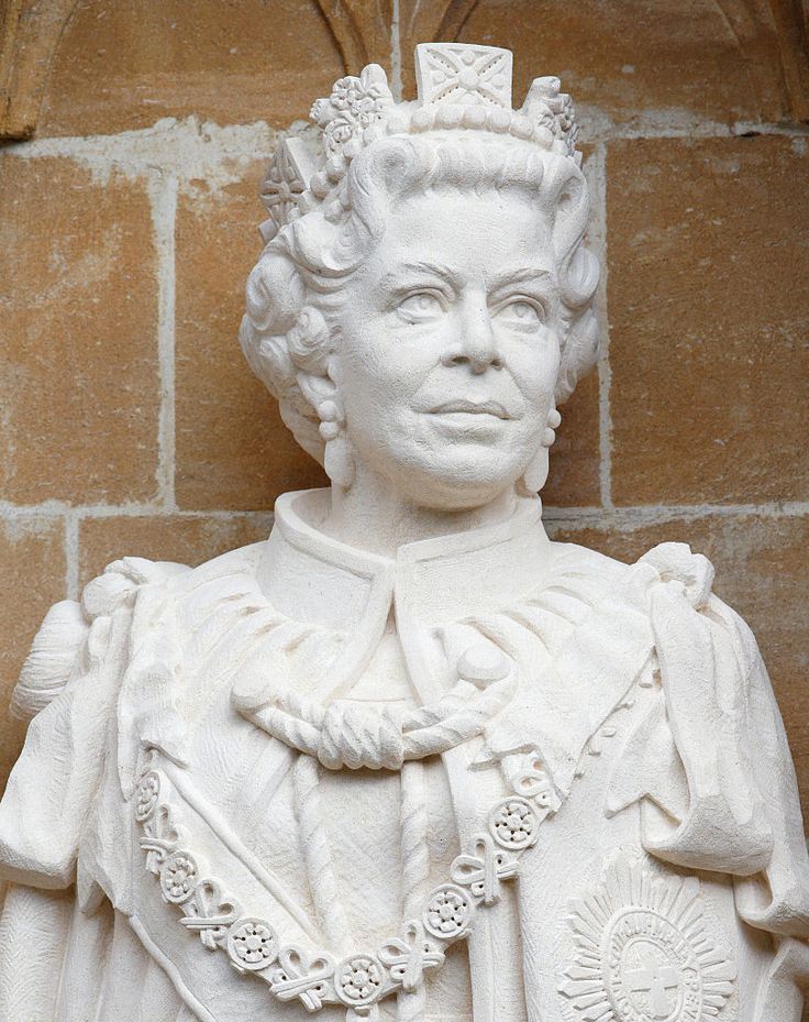 a white statue with a crown on it's head in front of a brick wall