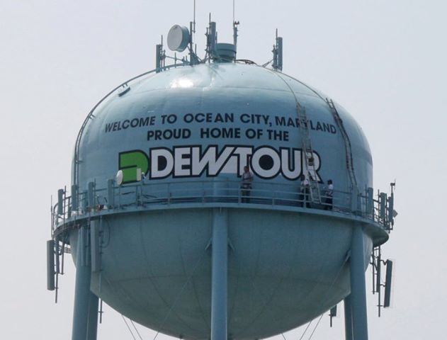 a large metal water tower with people standing on it's sides and the words dew tour written on its side