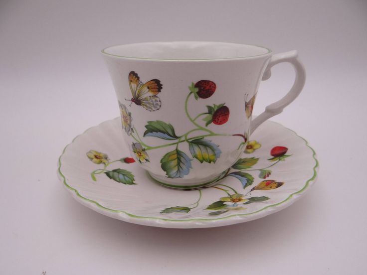 a coffee cup and saucer decorated with flowers, leaves and butterflies on a white background