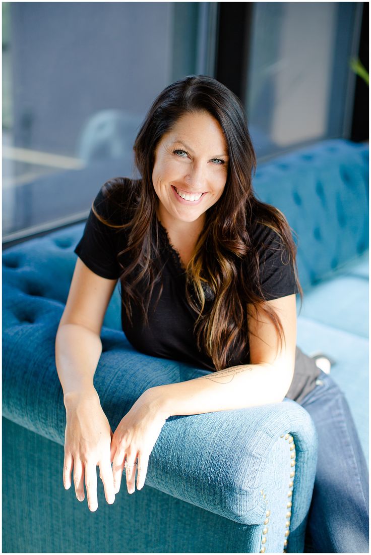 a woman sitting on top of a blue couch smiling at the camera with her arms crossed