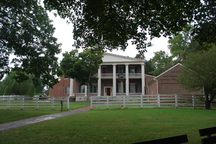 a large house sitting in the middle of a lush green field next to a wooden fence