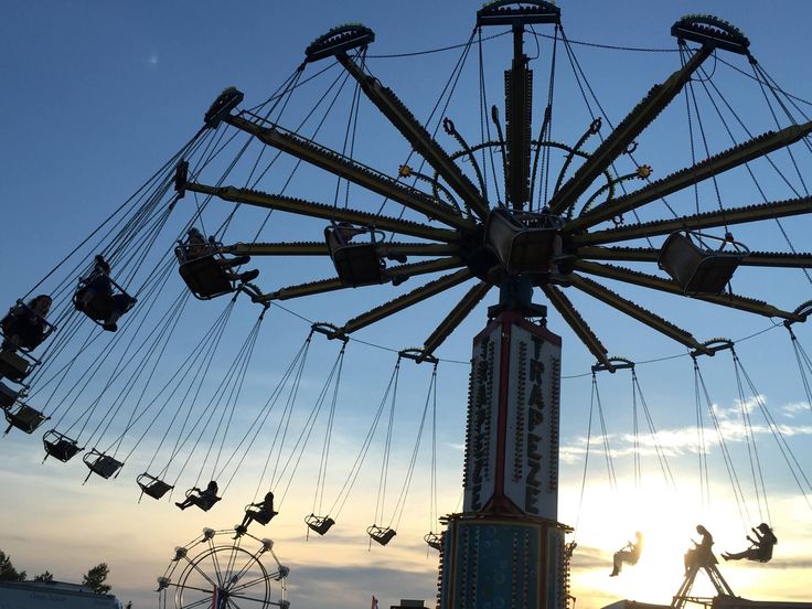 a carnival ride with people riding it at sunset or dawn in the background, as well as several roller coasters