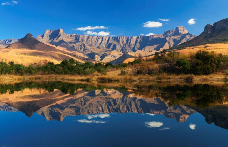 the mountains are reflected in the still water on the lake's surface, while clouds and blue sky reflect off the mountain tops