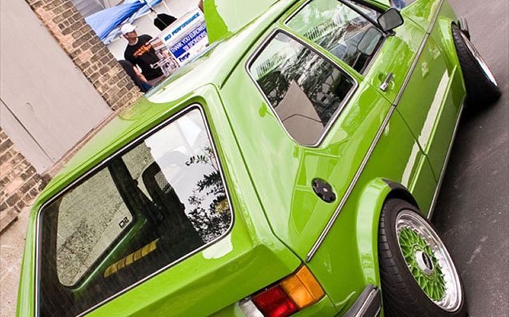 a green car parked on the side of the road next to a brick wall and sidewalk