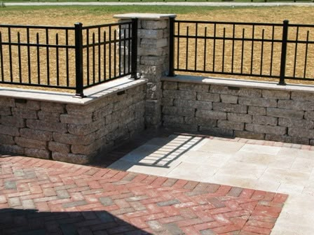 a brick wall with black iron railings on the top and bottom, in front of a grassy field