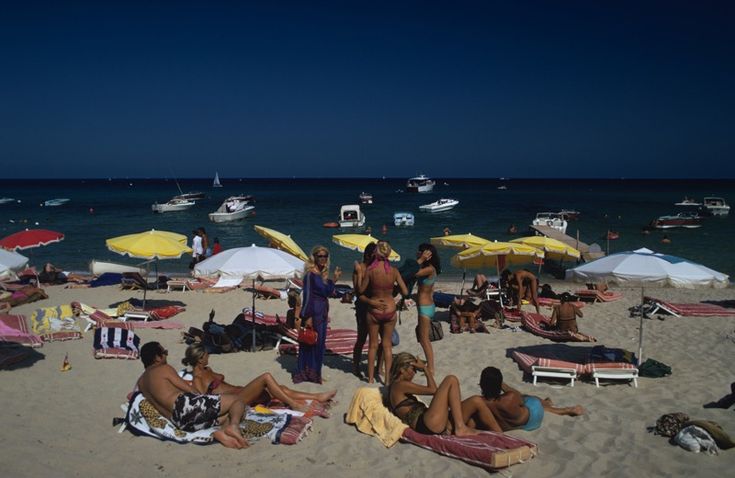 many people are sitting on the beach under umbrellas and sunbathers near the water