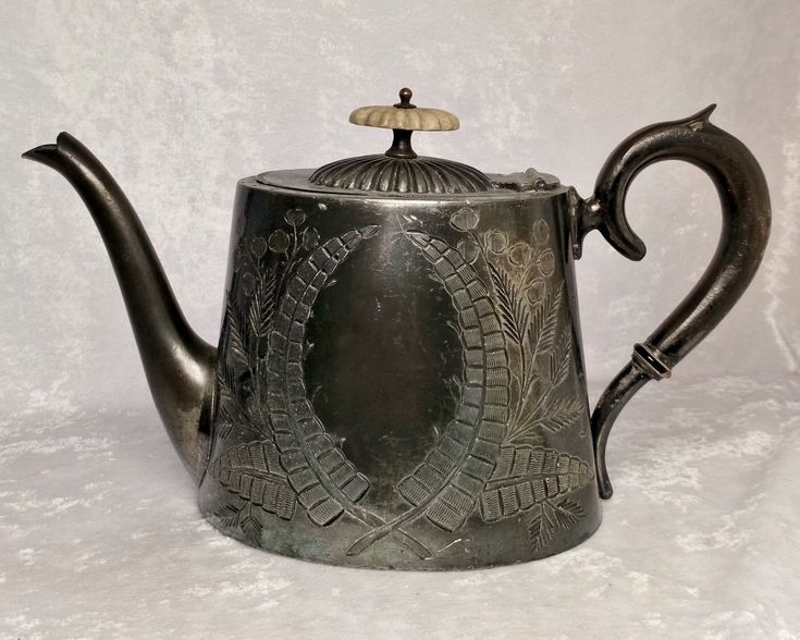 a silver teapot with an ornate design on the front and sides, sitting on a white surface