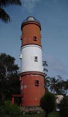 a large red and white tower sitting on top of a lush green field next to trees