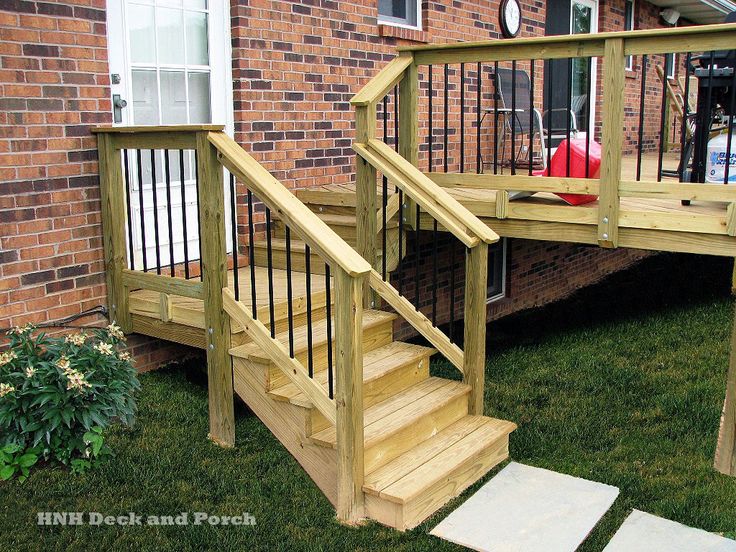 a wooden deck with steps leading up to the front door and back porch area, next to a brick building