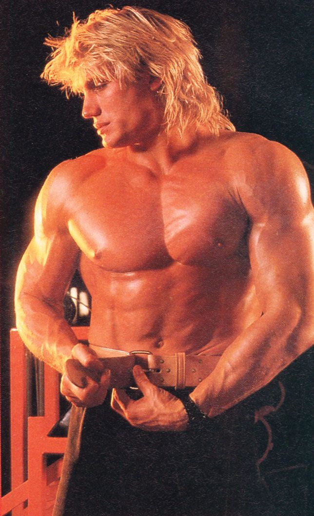 a man with long blonde hair and no shirt is posing for the camera while holding his hands in his pockets