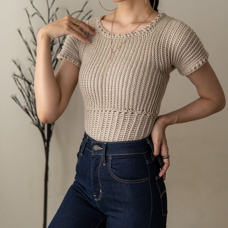 a woman in jeans and a knitted top poses for the camera with her hands on her hips