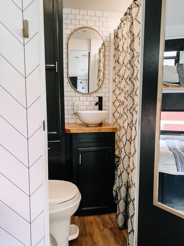 a white toilet sitting next to a sink in a bathroom under a mirror on top of a wooden floor