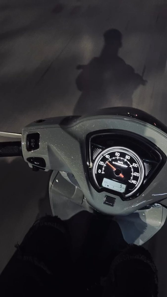 the dashboard of a motorcycle is shown in this close - up photo, with its driver's shadow on the ground