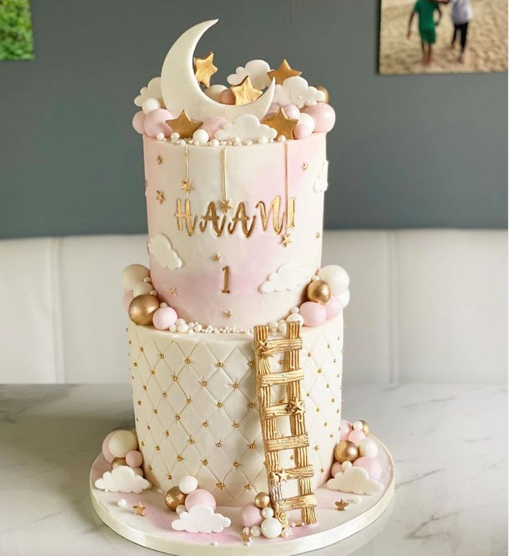 a three tiered cake is decorated with pink and white icing, gold decorations, and stars