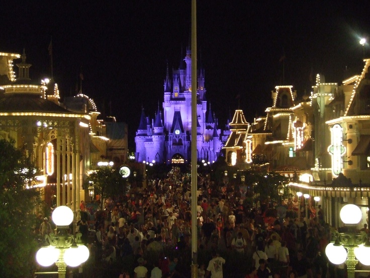 a crowd of people walking down a street in front of a building with lights on it