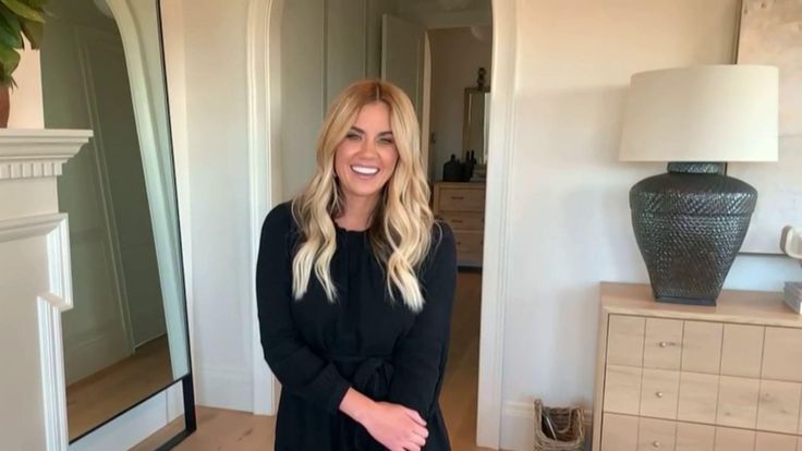 a woman standing in front of a mirror smiling at the camera with her hand on her hip