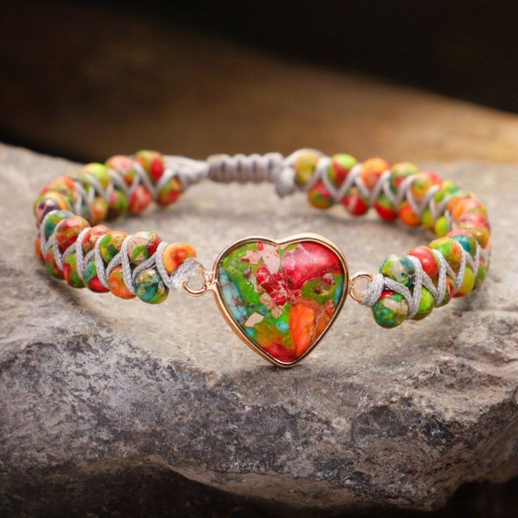 a heart shaped glass beaded bracelet sitting on top of a rock