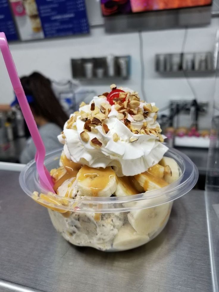 an ice cream sundae with bananas and nuts in a plastic container on a counter